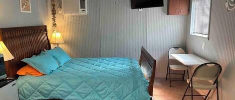 Een slaapkamer met een bed, een bureau, een stoel, een plafondventilator, airconditioning en een televisie.