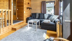 A cozy cabin interior with a wooden exterior, a gray sofa with cushions, a white coffee table, and a large window with curtains. - Kuusipirtti by Interhome (Puolanka)