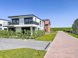 A modern two-story house with a balcony, a paved driveway, and a well-maintained lawn.