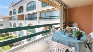A balcony with a table set for dining, overlooking a building with multiple balconies and a garden.
