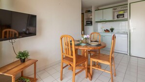 A compact living space with a dining area featuring a wooden table and chairs, a small bench, and a flat-screen TV mounted on the wall.