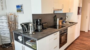 Una cocina moderna con armarios blancos, encimera negra, cafetera y microondas.