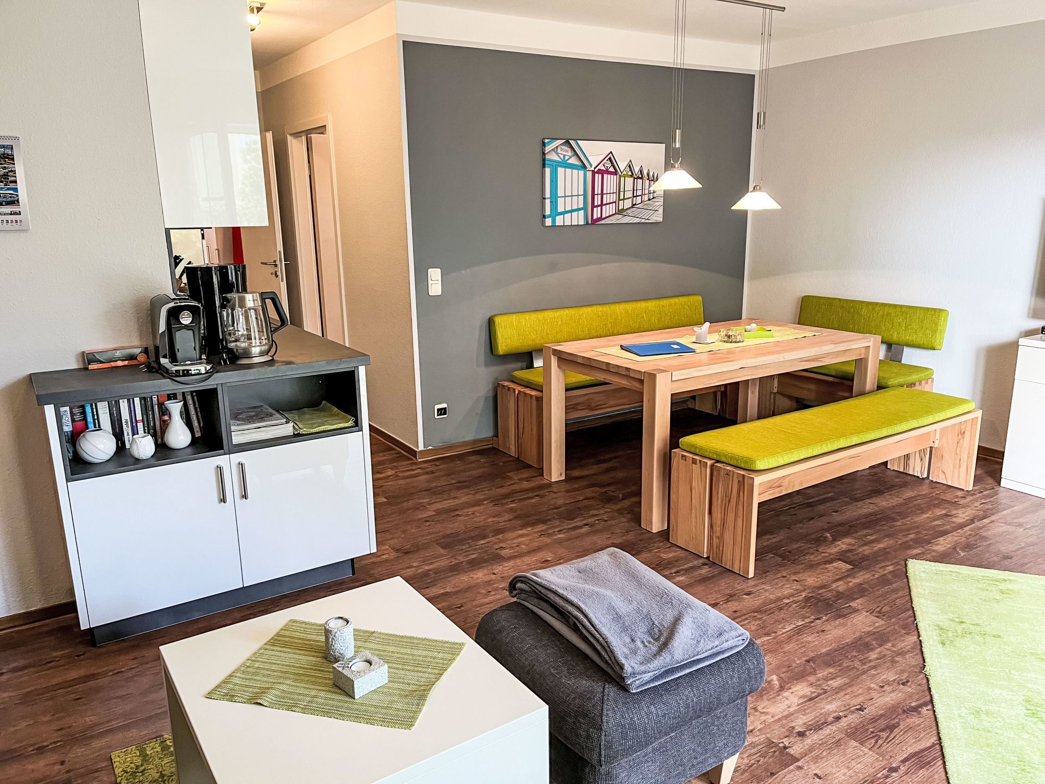 Ein modernes Wohnzimmer mit einem Holztisch, einer gepolsterten grünen Bank und einer weißen Kommode mit Büchern und Dekoration.