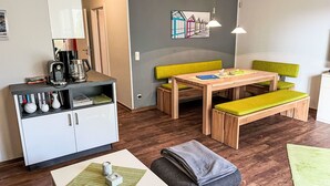 Una sala moderna con una mesa de madera, un banco acolchado verde y un mueble blanco con libros y objetos decorativos.