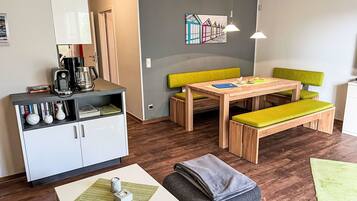 Ein modernes Wohnzimmer mit einem Holztisch, einer gepolsterten grünen Bank und einer weißen Kommode mit Büchern und Dekoration.