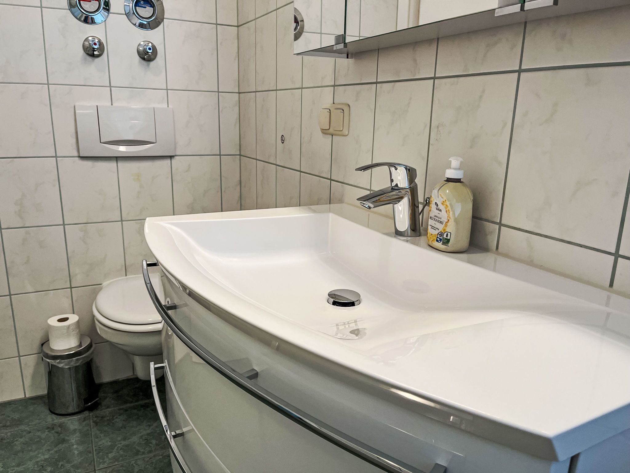 A modern bathroom with a large white sink, a toilet, and a trash can.
