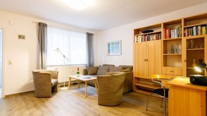 Een goed verlichte woonkamer met een bank, stoelen, een salontafel en een boekenkast.