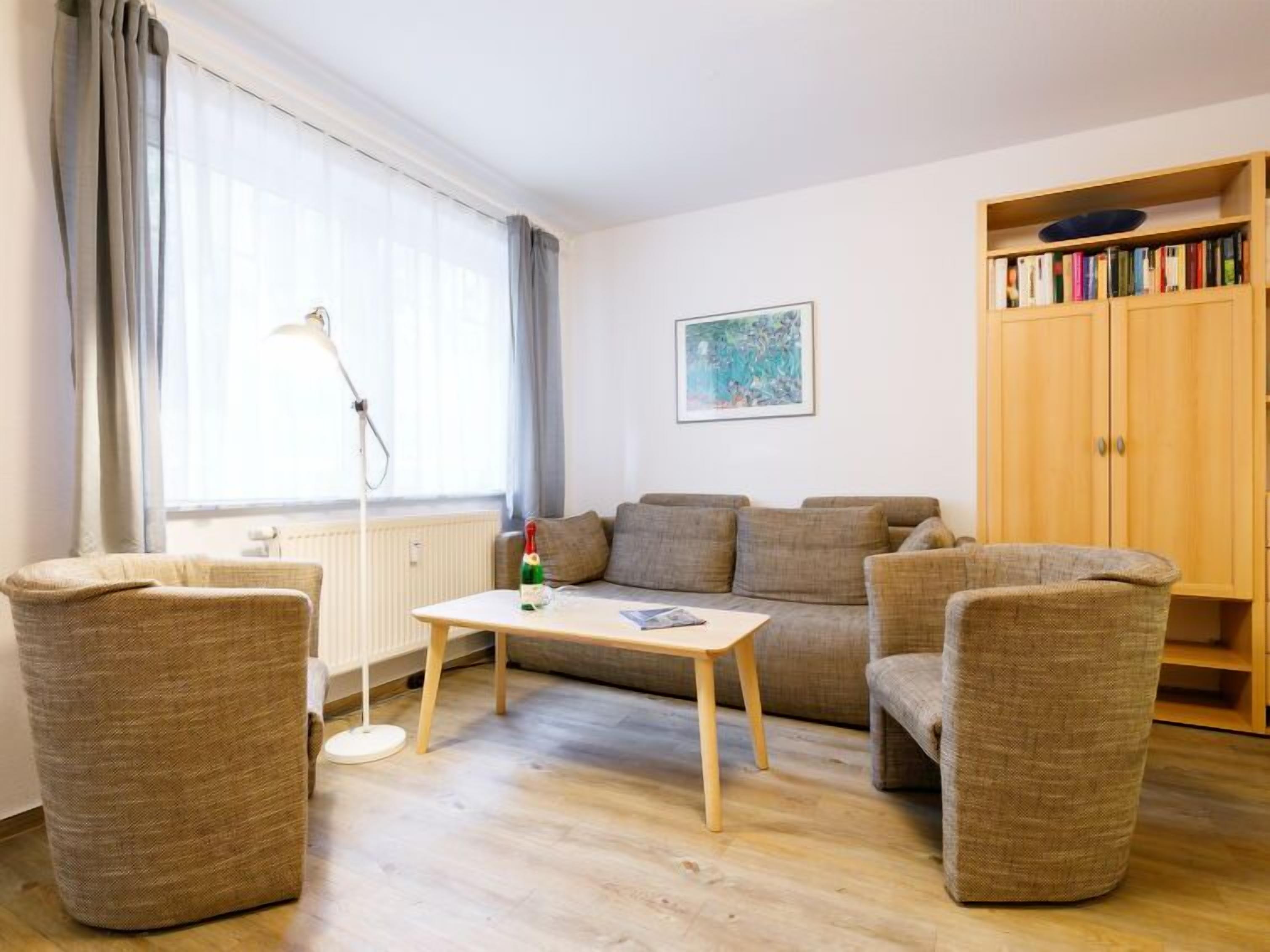 Kodikas olohuone, jossa on sohva, kaksi nojatuolia, sohvapöytä, kirjahylly ja patteri.