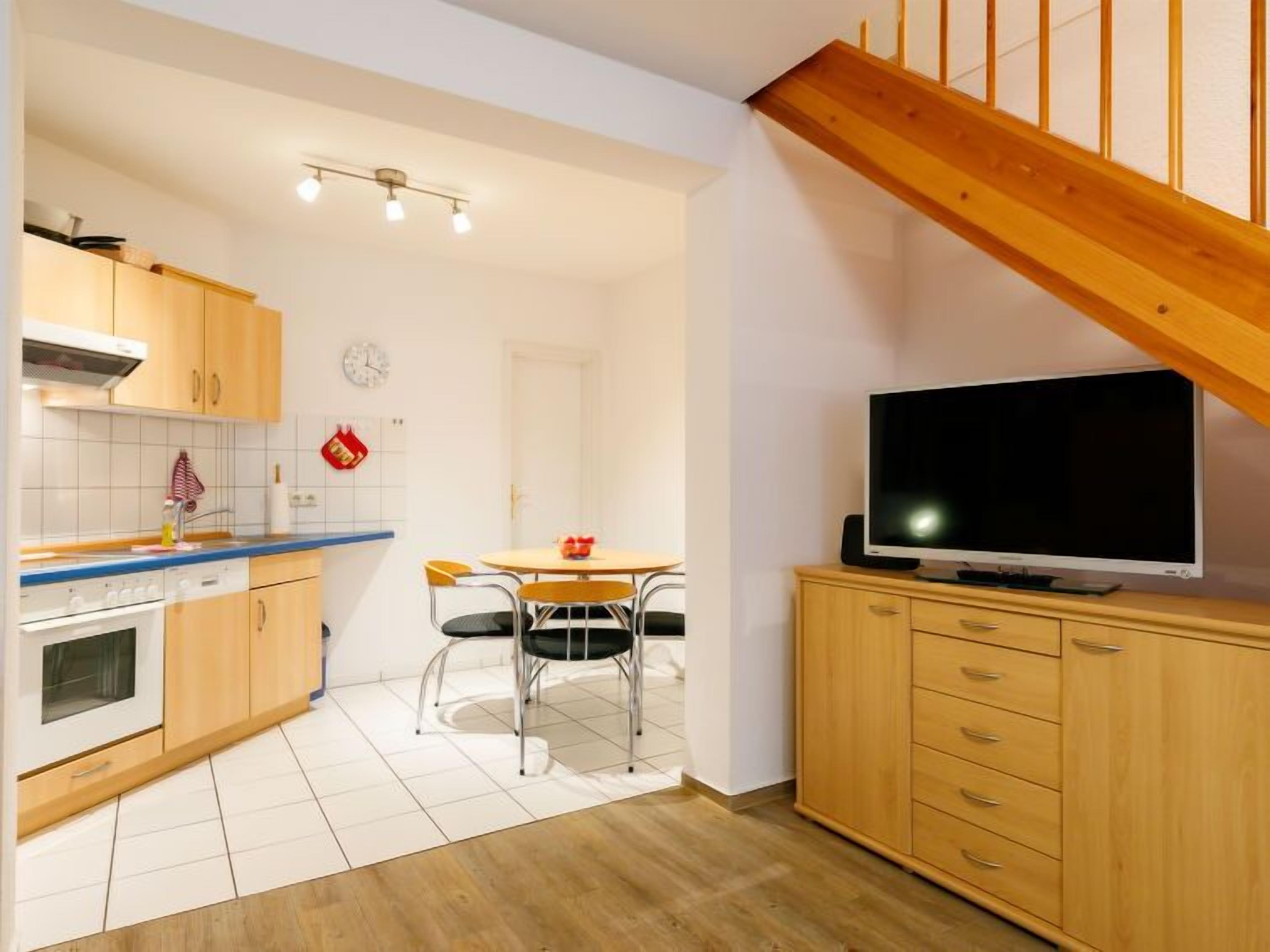 Une cuisine de taille réduite, dotée de meubles en bois, d’une cuisinière et d’un coin repas avec des chaises.