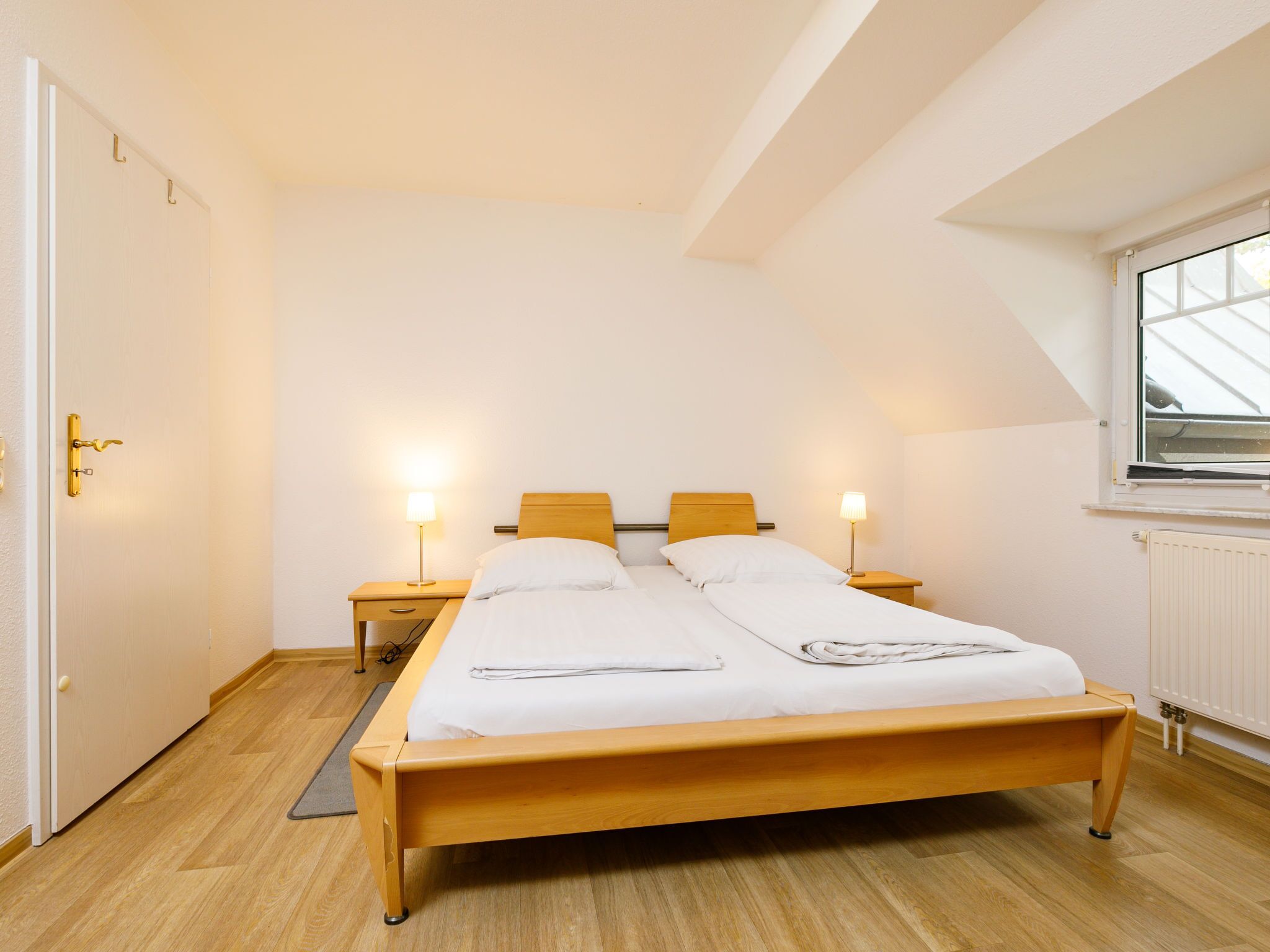 Ein Zimmer mit einem Einzelbett, einem Holzkopfstück, zwei Nachttischen mit Lampen, einem Fenster mit Aussicht und einer Heizung.