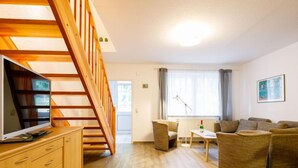 Een moderne woonkamer met een houten trap, een flatscreen televisie, een zithoek en een eethoek.