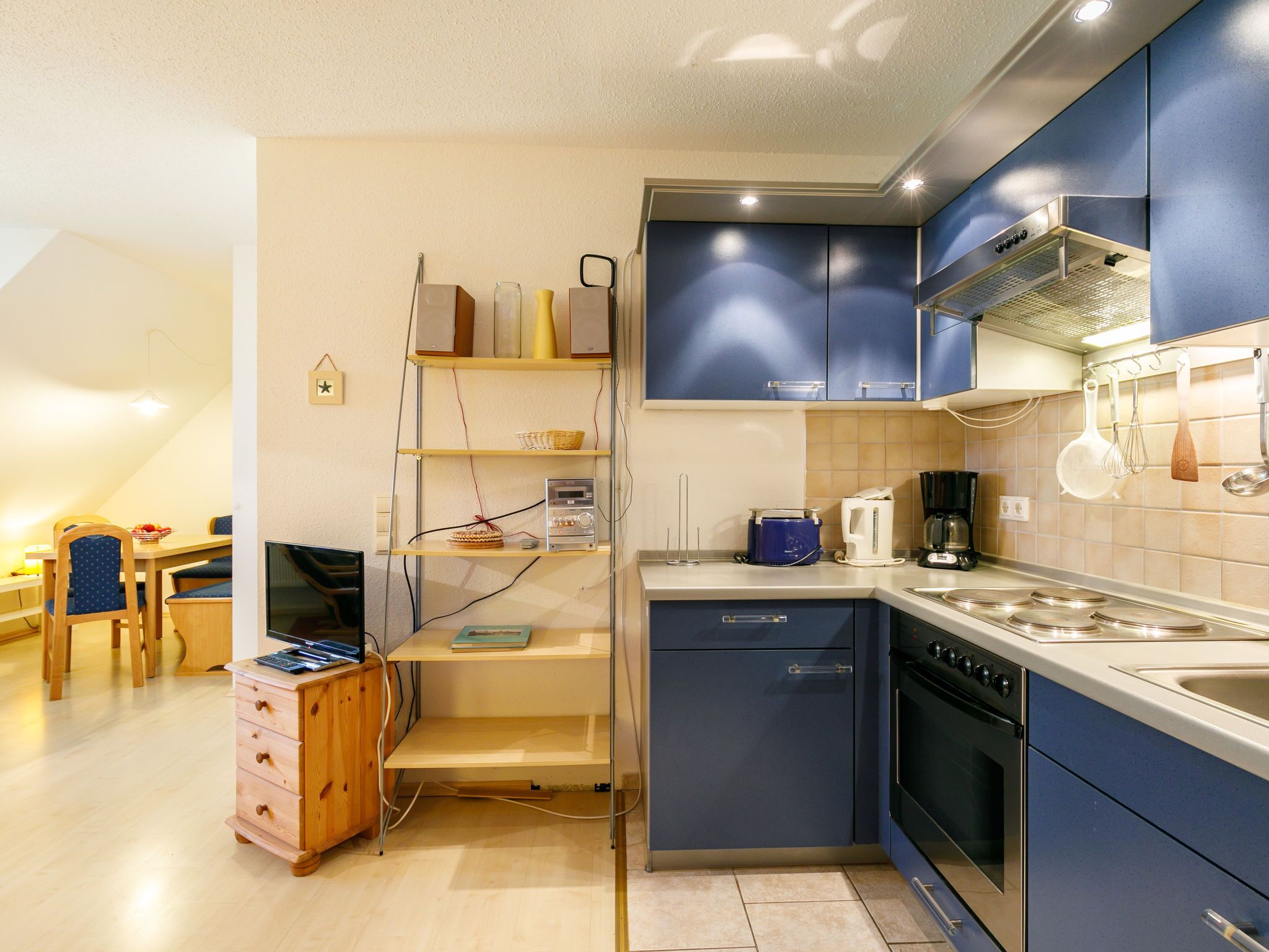 A compact kitchen with blue cabinets, a stove, a sink, and a dining area with a table and chairs.