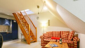 Un loft acollidor amb una escala de fusta, un sofà amb veta vermella i blanca, taula de dinar i zona de cuina.