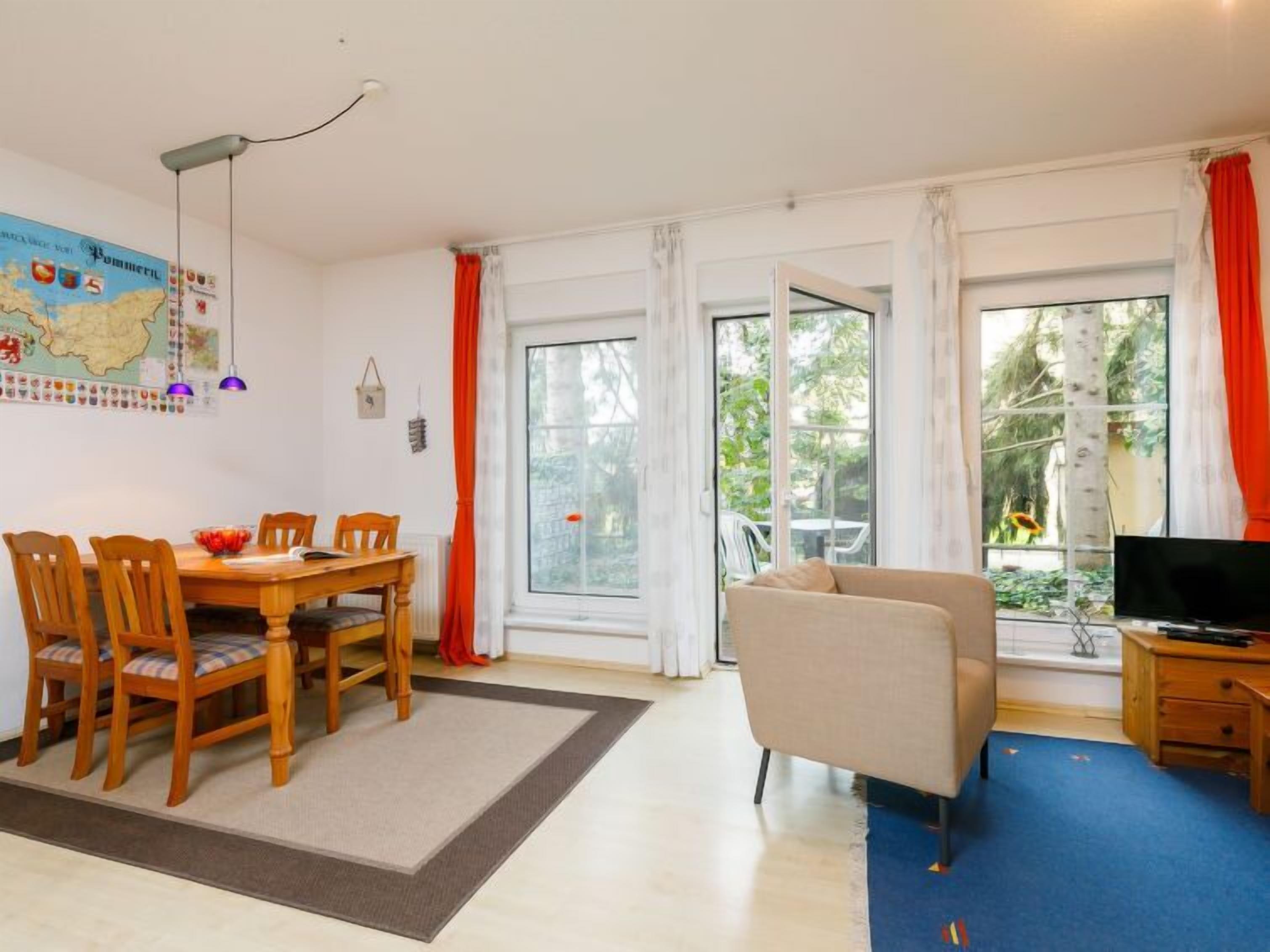 A living room with a dining area, large windows, a sofa, and a TV.
