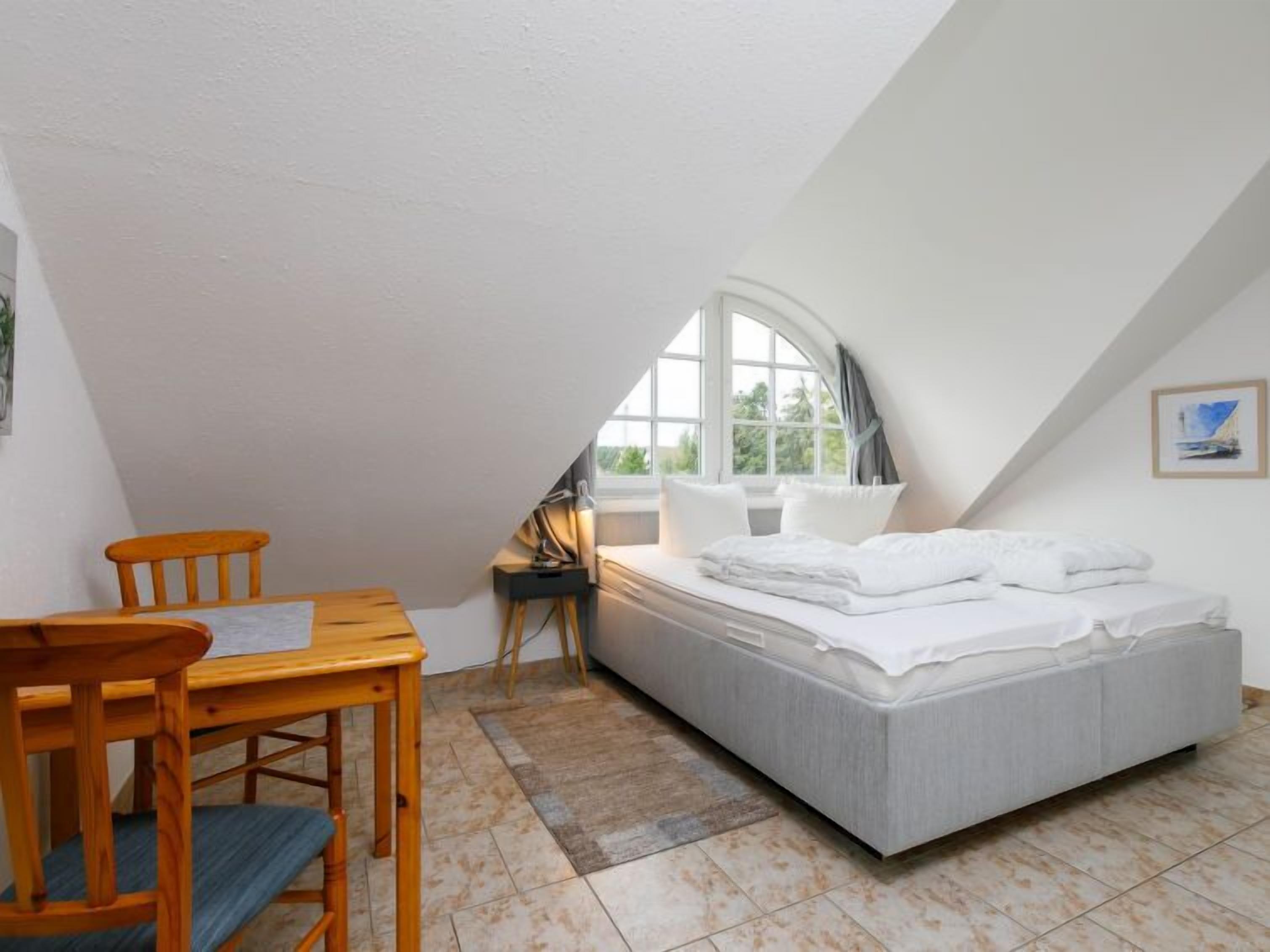A small, well-lit attic bedroom with a bed, a desk, and a chair.