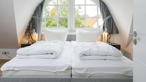 A bedroom with two beds, a large arched window, and a view of trees and a house. - Achterwasser App. 3 by Interhome (Zempin)