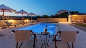 A pool area with lounge chairs and umbrellas, a table with a bottle, and a building in the background.