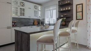 A modern kitchen with white cabinetry, a central island with bar stools, and decorative items on shelves.