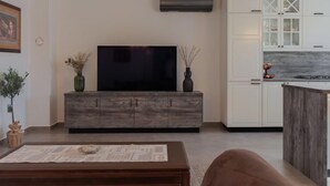 A modern living room with a flat-screen TV, a wooden cabinet, and a dining area with a kitchen in the background.