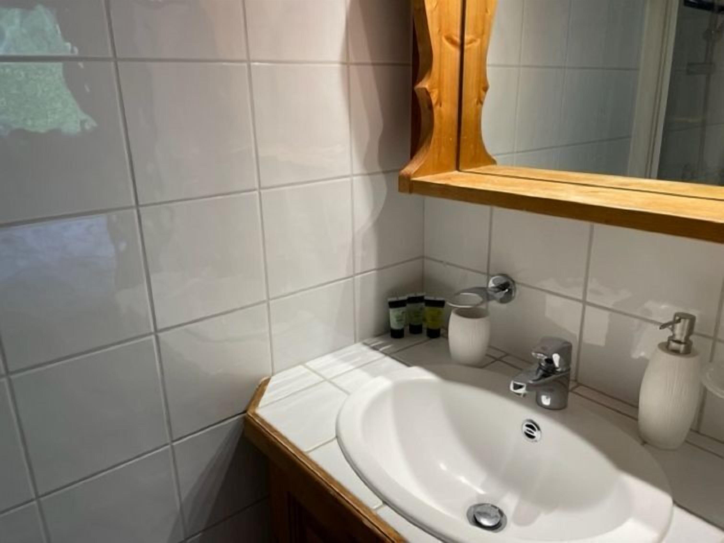 Casa de banho com lavatório branco, espelho com moldura de madeira e pequena prateleira com artigos de higiene pessoal.