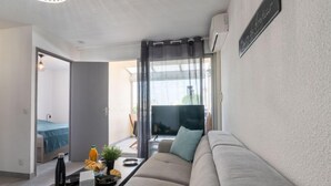 A modern living room with a sofa, a coffee table, and a TV. There's a balcony with a view.
