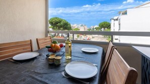 A balcony with a table set for dining, a bottle of wine, and a bowl of fruit.