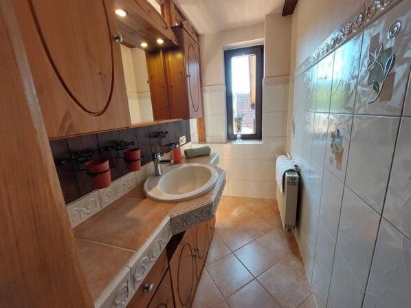 Une salle de bain avec un meuble-lavabo en bois, un évier et un miroir. Il y a une fenêtre donnant sur l’extérieur.
