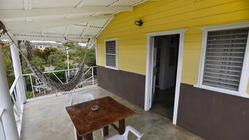 A yellow building with a covered porch, a hammock, and a table with chairs.