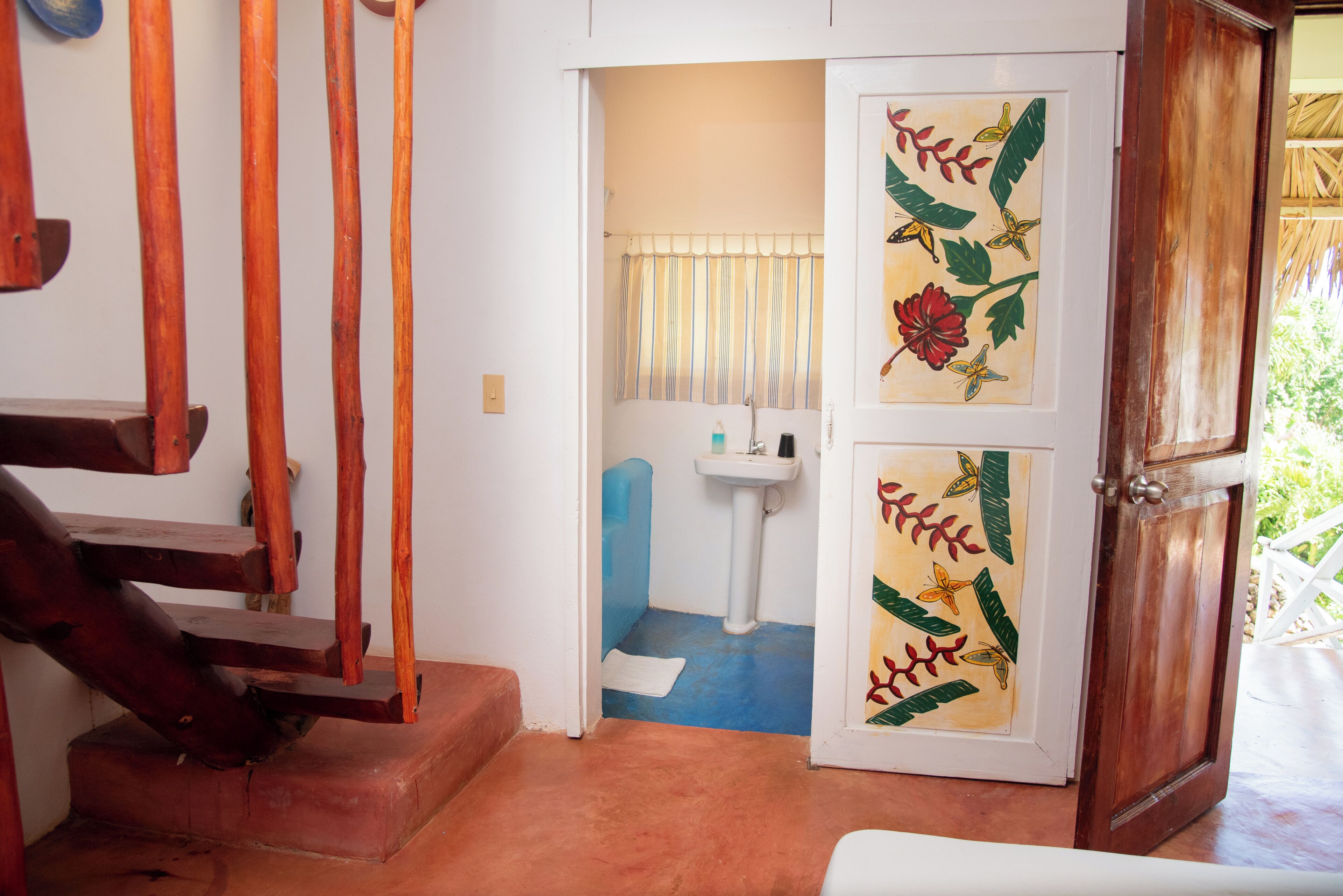 Eine Holztreppe führt zu einem Badezimmer mit einem Waschbecken und einer Tür mit floralem Dekor.