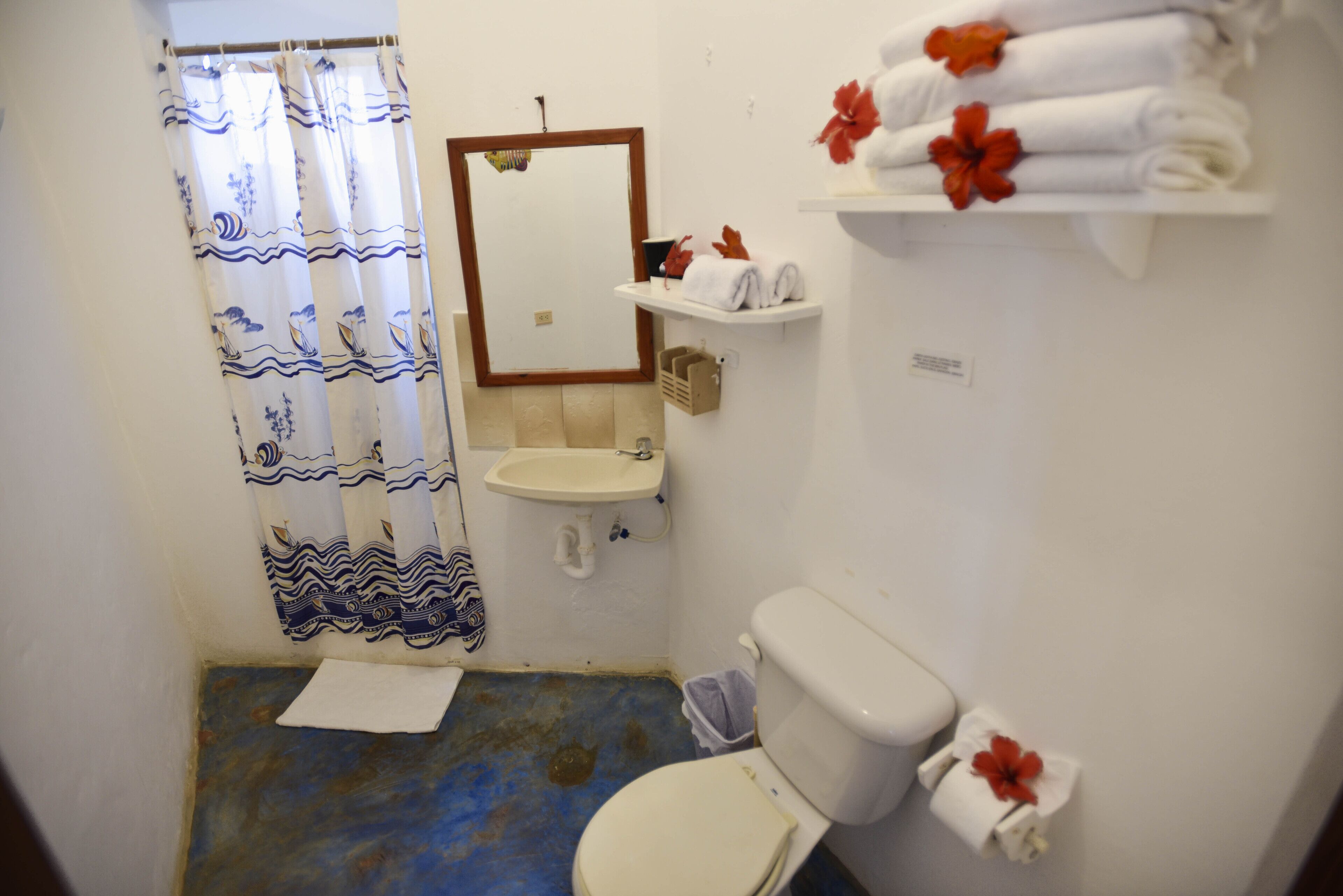 A small bathroom with a toilet, sink, and shower curtain. There are towels and toiletries on the wall.