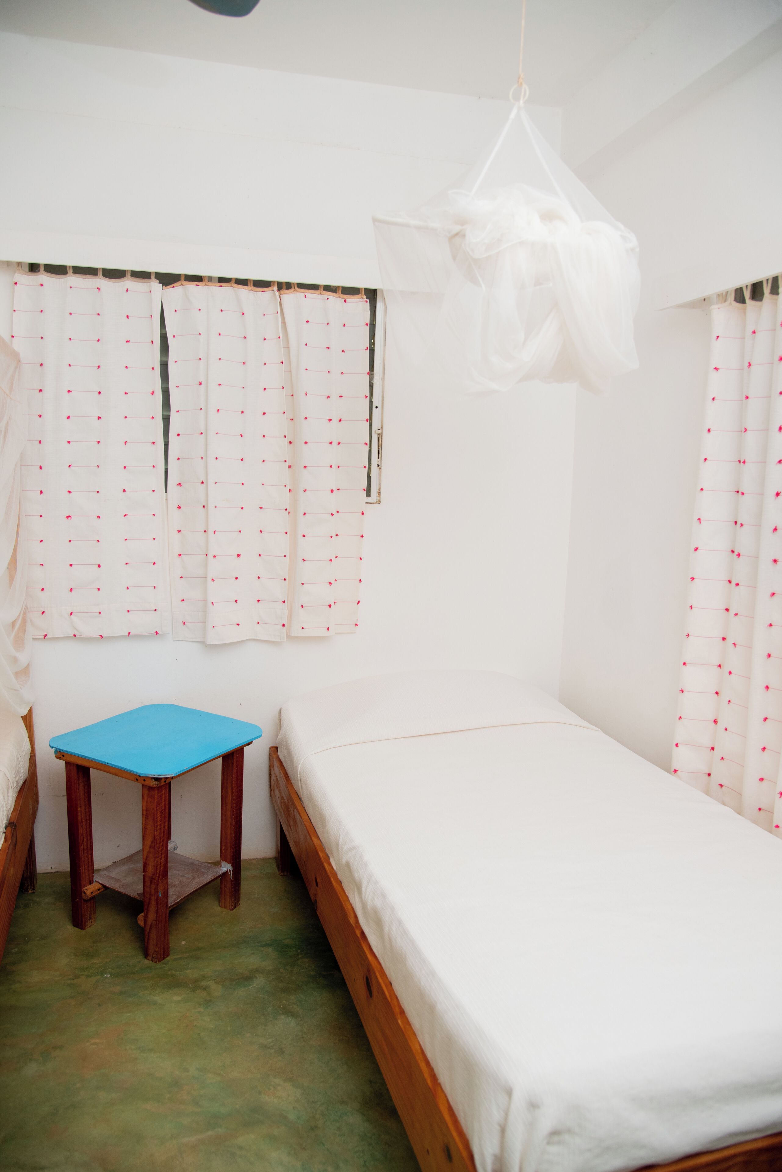 A small, simple room with a single bed, a small table, and curtains with a pattern.