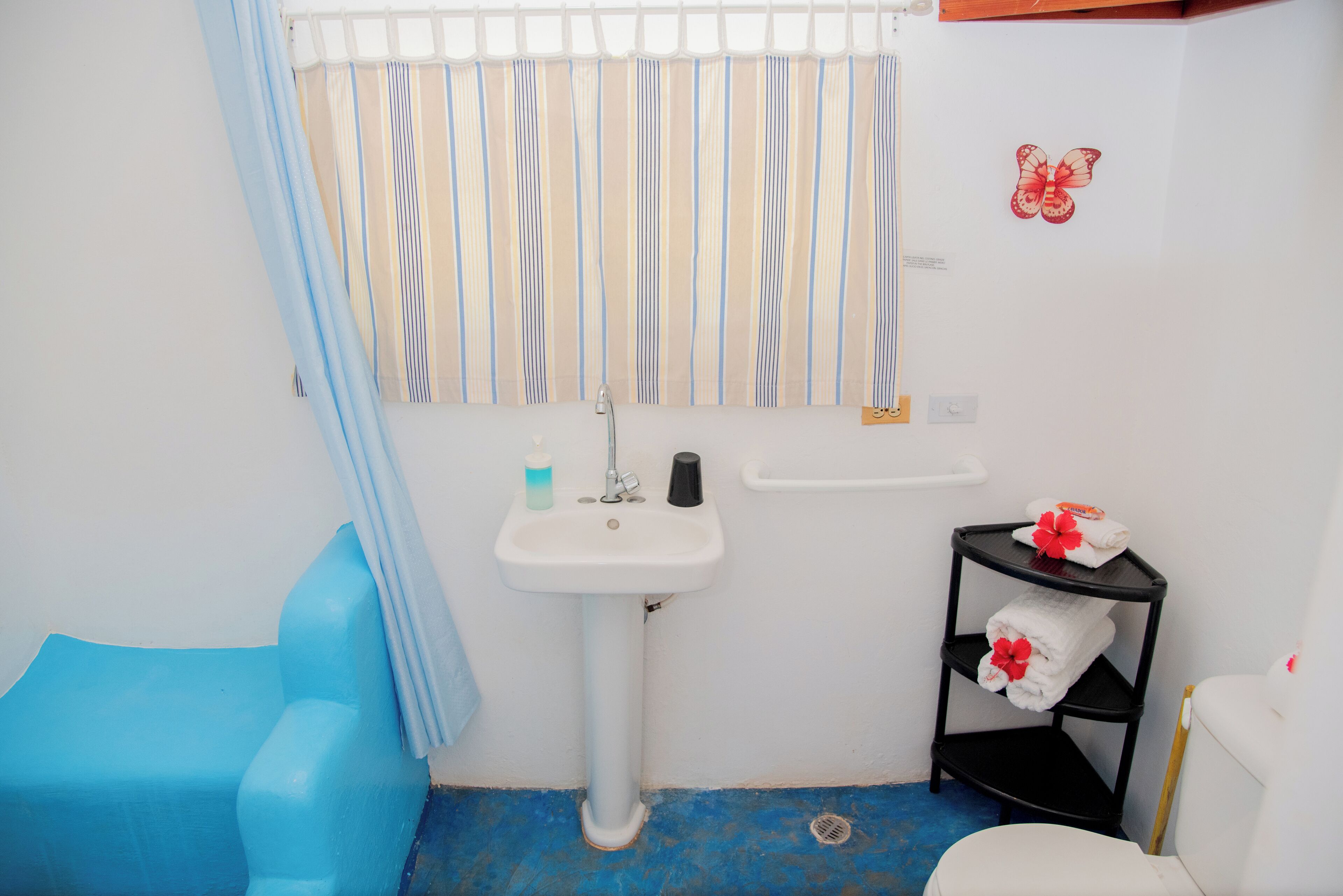 A bathroom with a blue bathtub, a white sink, striped curtains, and a towel rack with towels.