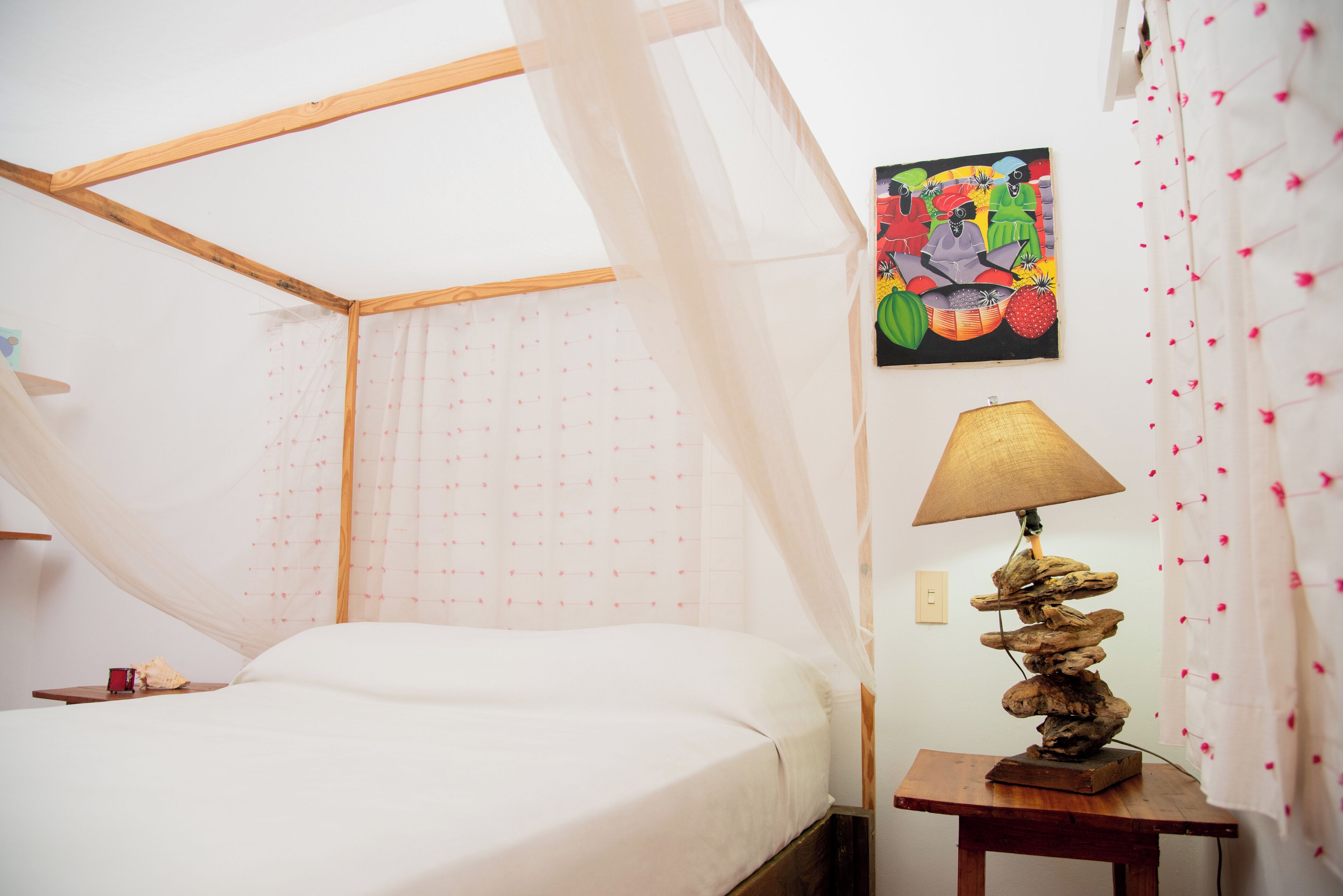 Una camera da letto con un letto, un comodino con una lampada, un quadro appeso al muro e una tenda con motivo floreale.