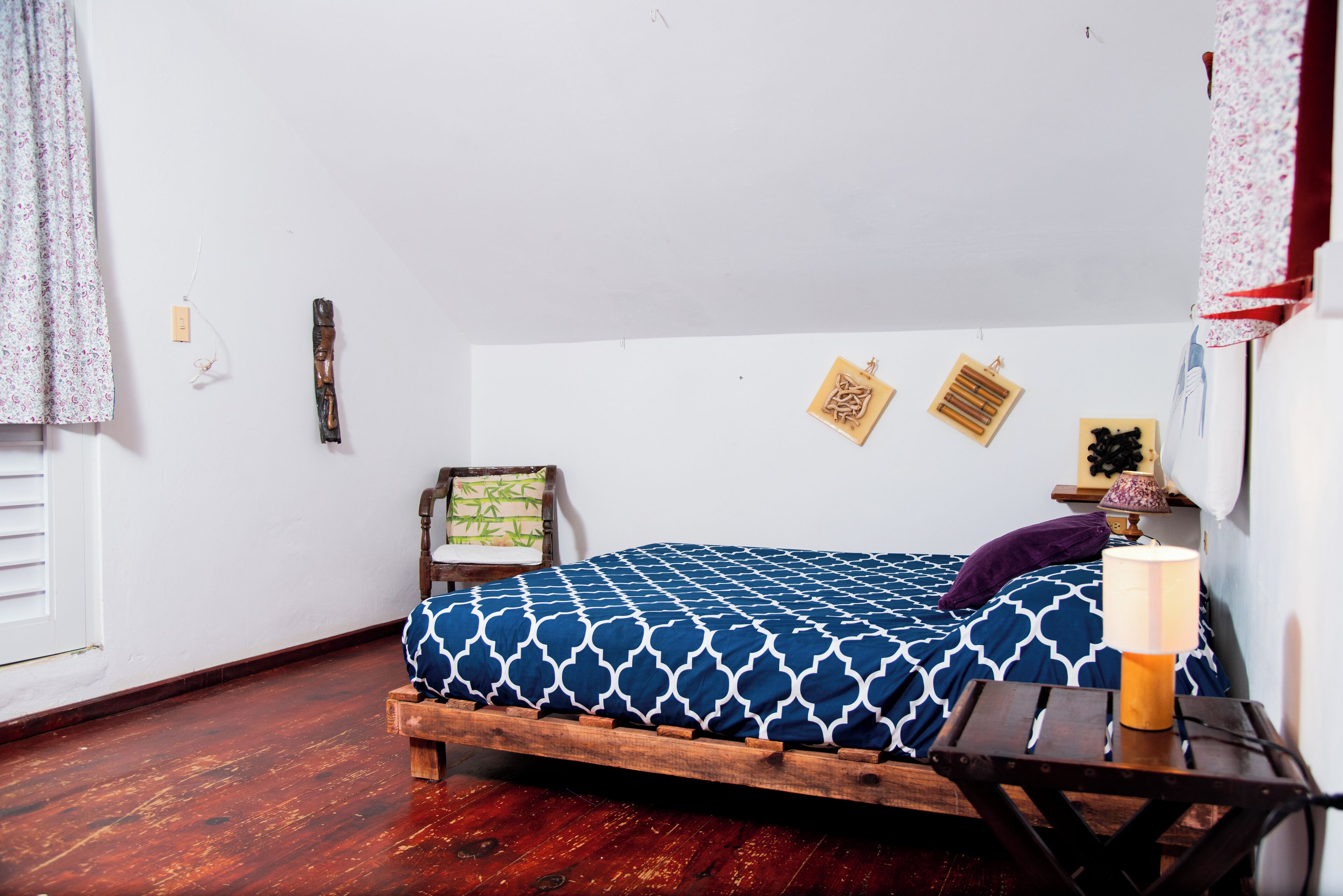 A room with a wooden bed, a small table with a lamp, and a wall with framed pictures.