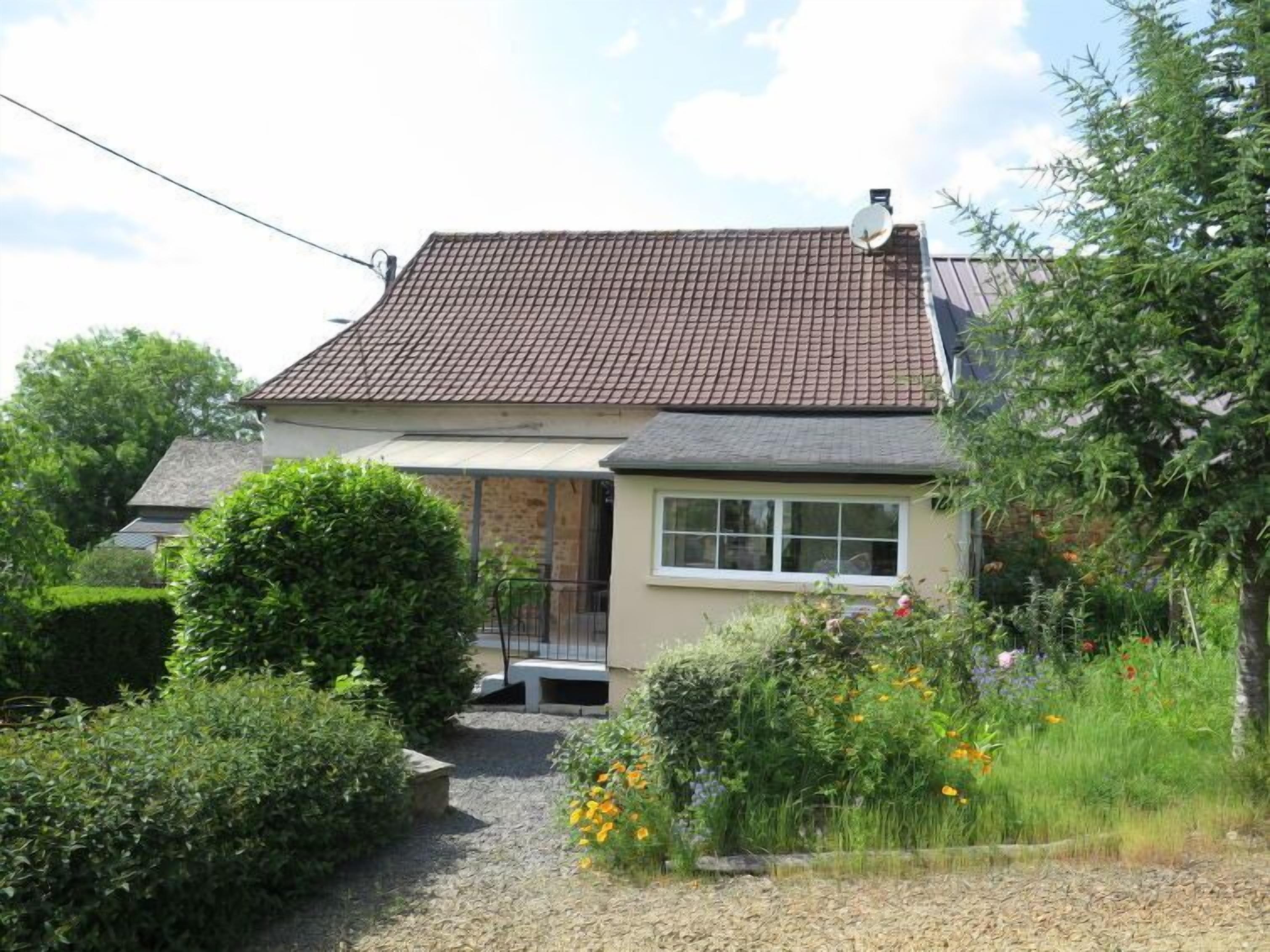 A single-story house with a tiled roof, a front porch, and a garden with various plants and flowers.