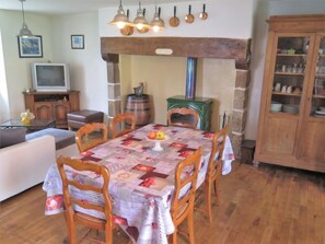 A dining area with a quilted tablecloth, wooden chairs, a vintage stove, and a television in the background.