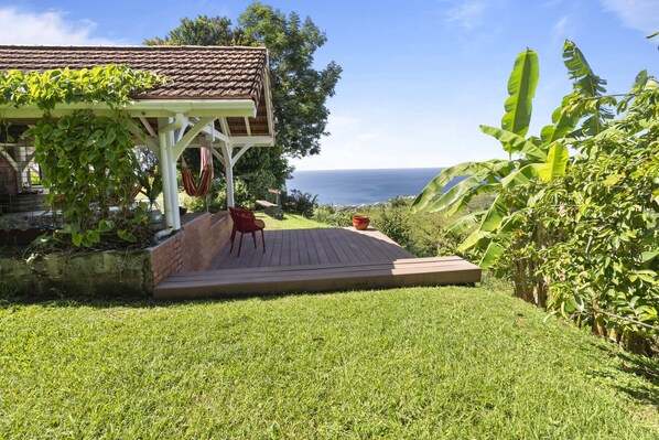 Un espacio de estar al aire libre con techo y vista al océano, una terraza de madera y exuberante vegetación.