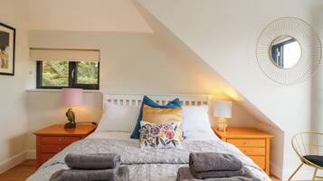 A bedroom with a bed, pillows, a nightstand, a lamp, a mirror, and a window.