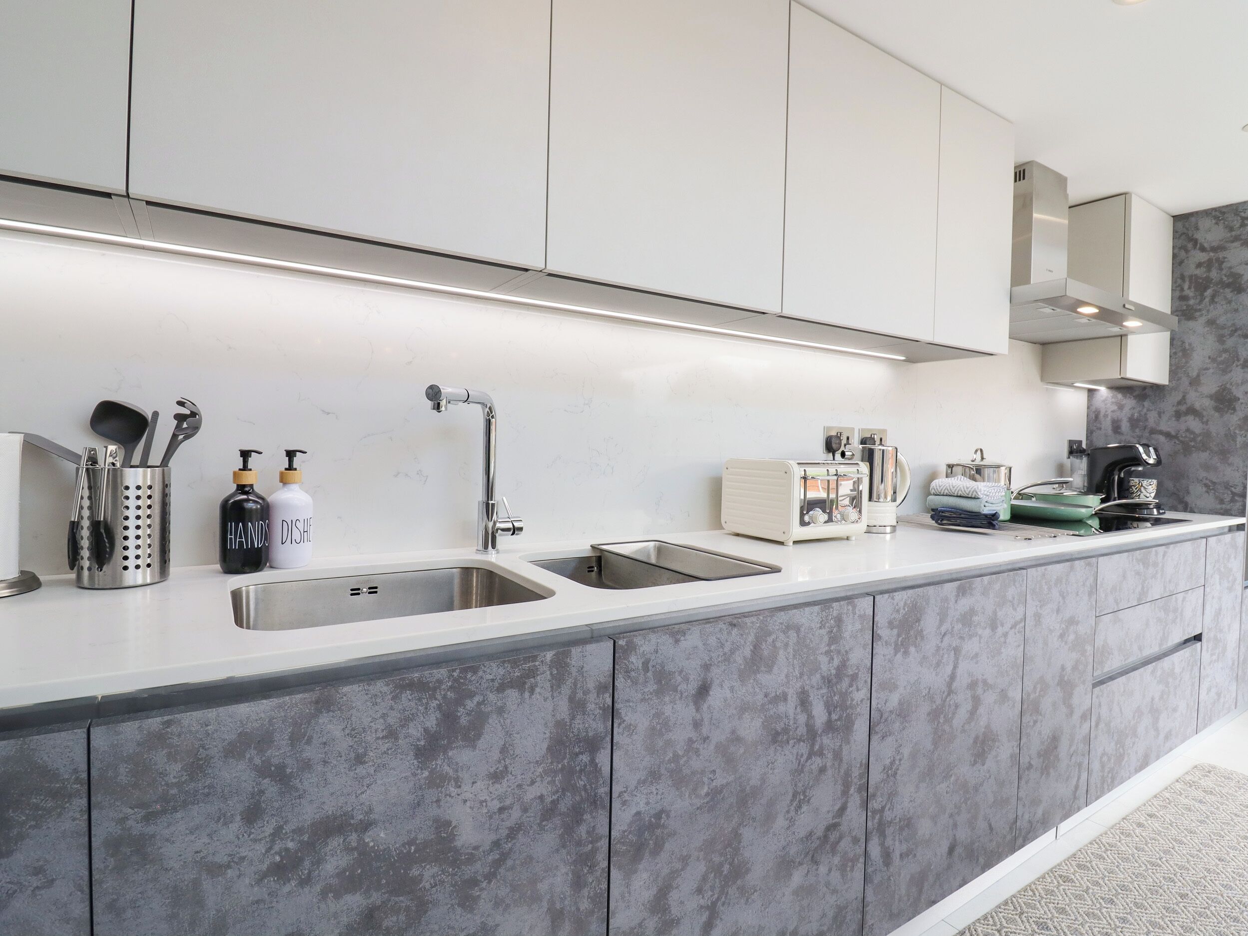 Una cocina moderna con dos fregaderos, utensilios de acero inoxidable, un tostador y una cafetera.