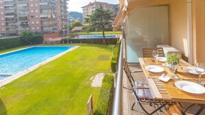 A balcony with a dining table set for two, overlooking a swimming pool and a well-maintained lawn. - Apartment Libra by Interhome (Santa Susanna)