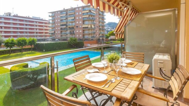 A balcony with a table set for dining, overlooking a swimming pool and a view of surrounding buildings. - Apartment Libra by Interhome (Santa Susanna)