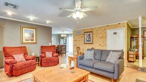 A living room with a wooden ceiling, a ceiling fan, a grey sofa, two red armchairs, a wooden coffee table, and a patterned rug. - Lawton Home w/ Deck, Near Casinos + Museums! (Lawton)
