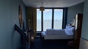Ett hotellrum med en säng, ett badrum med badkar, en värmare och ett stort fönster med utsikt.