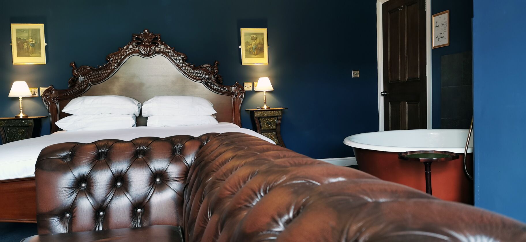 Quarto com uma cama grande, duas mesas de cabeceira com luminárias, cabeceira de madeira e um sofá marrom espaçoso.