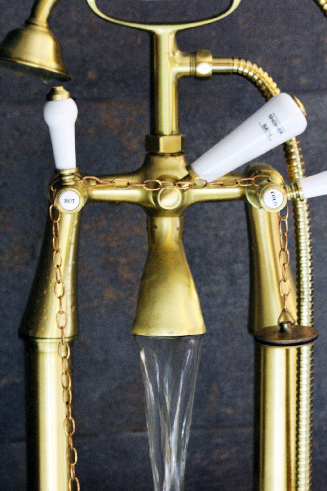 A brass water spigot with a clear glass spout and a white handle.