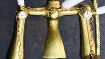 A brass water spigot with a clear glass spout and a white handle.
