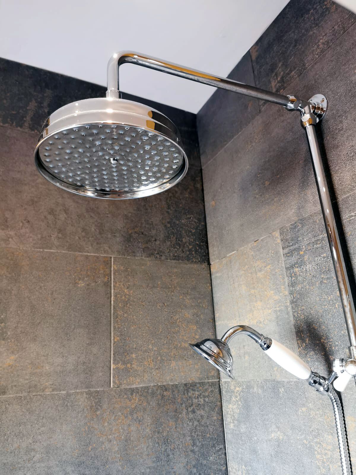 A shower with a handheld attachment and a fixed showerhead.