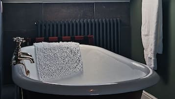A bathroom with a freestanding bathtub, a skylight, a towel rack, and a radiator.