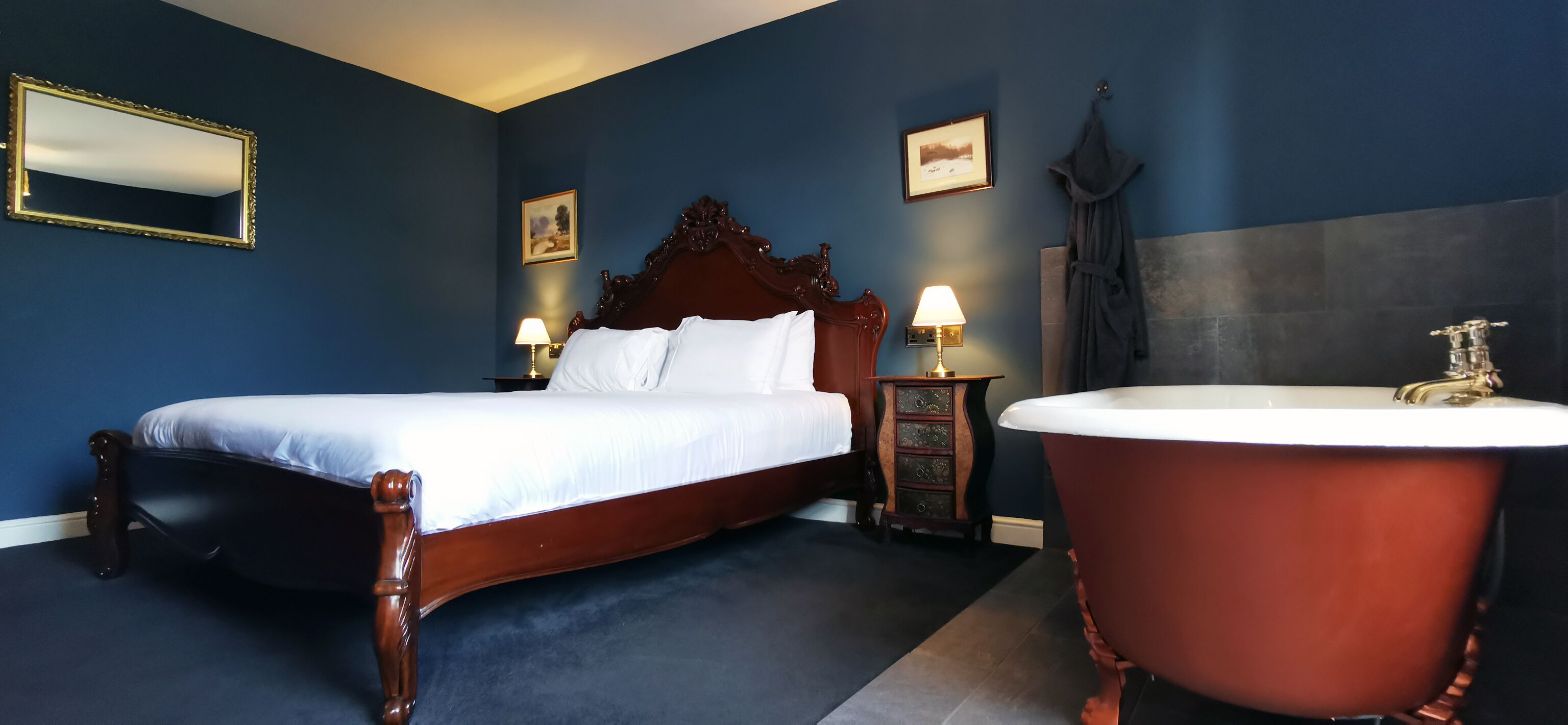 Ein Schlafzimmer mit einem großen Bett, einem Holzkopfschild, einer Badewanne im Vintage-Stil und einem Nachttisch mit einer Lampe.