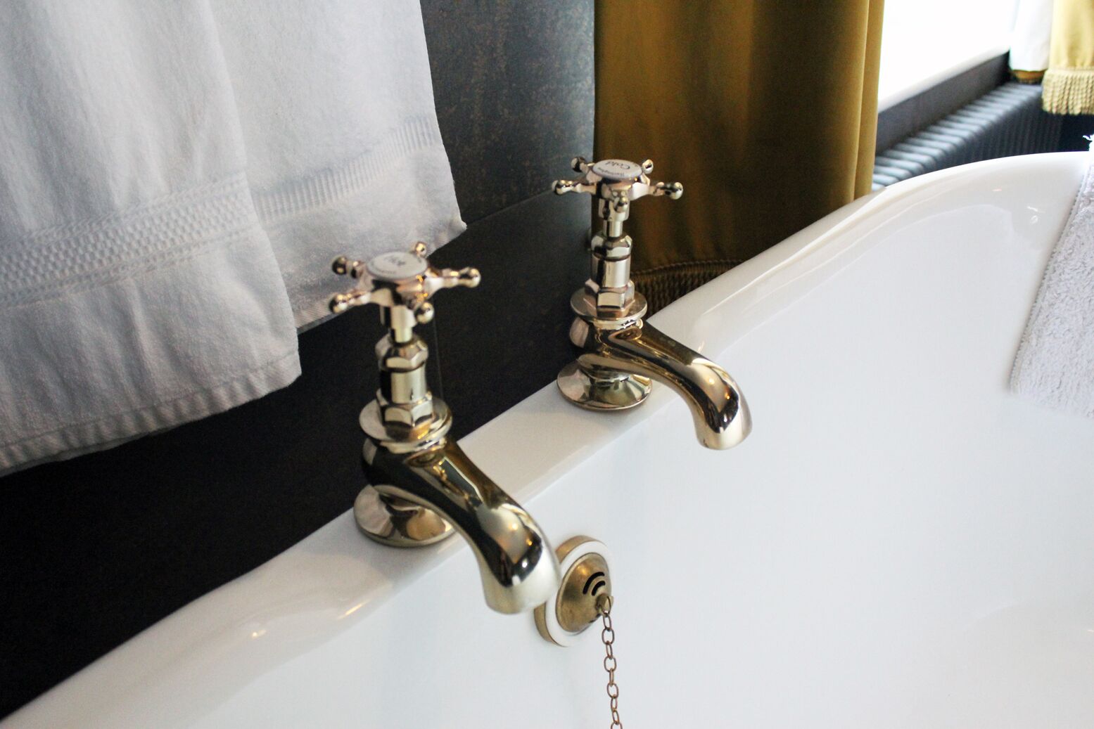 A bathroom with a white bathtub, two chrome faucets, and a towel hanging on a dark-colored towel rack.